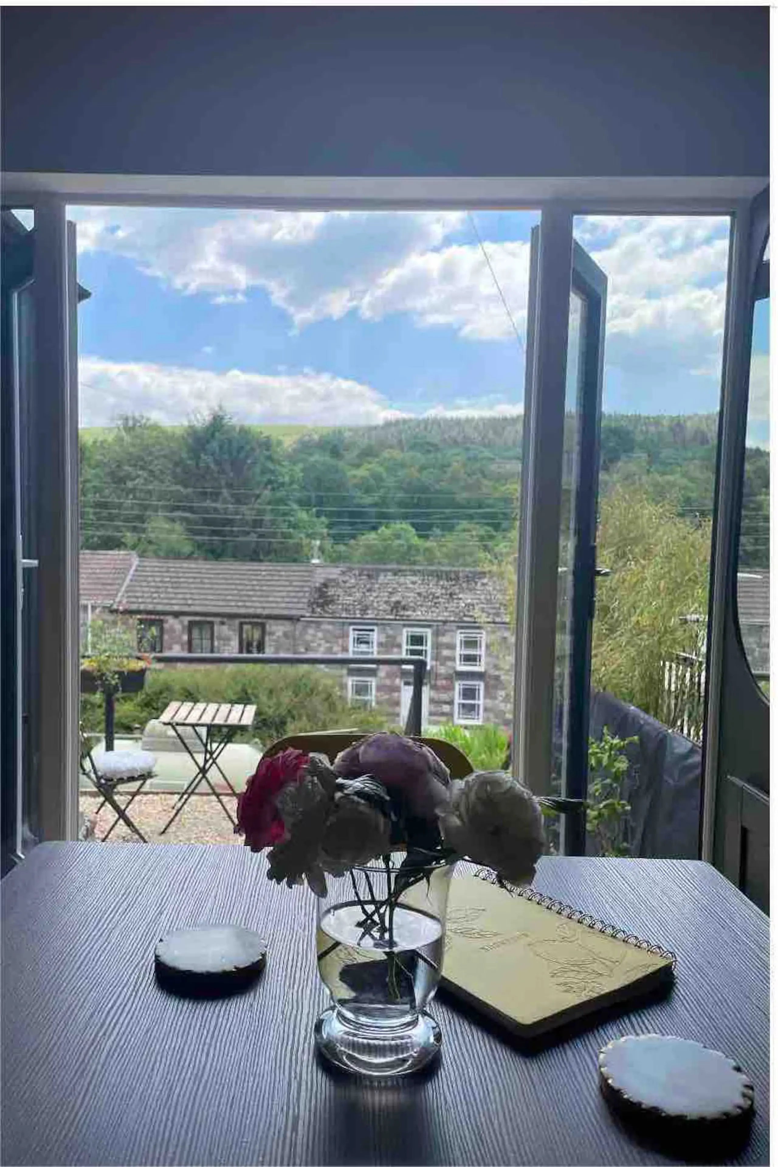 Dining table with fresh flowers in front of open French doors overlooking the village and forest